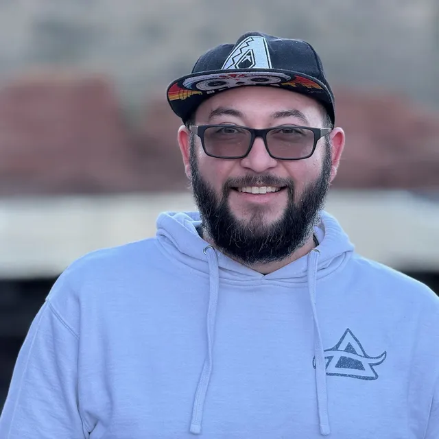 OnBrand smiling in a snapback cap and a pale grey hoodie, with red rock cliffs blurred behind him